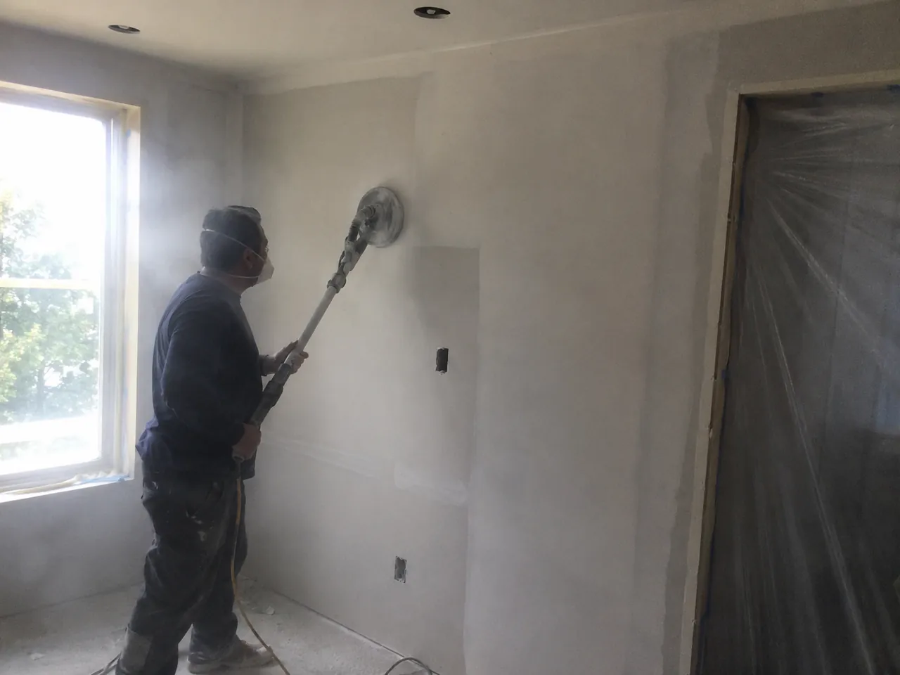 Sanding dried joint compound on a wall with dust in the air