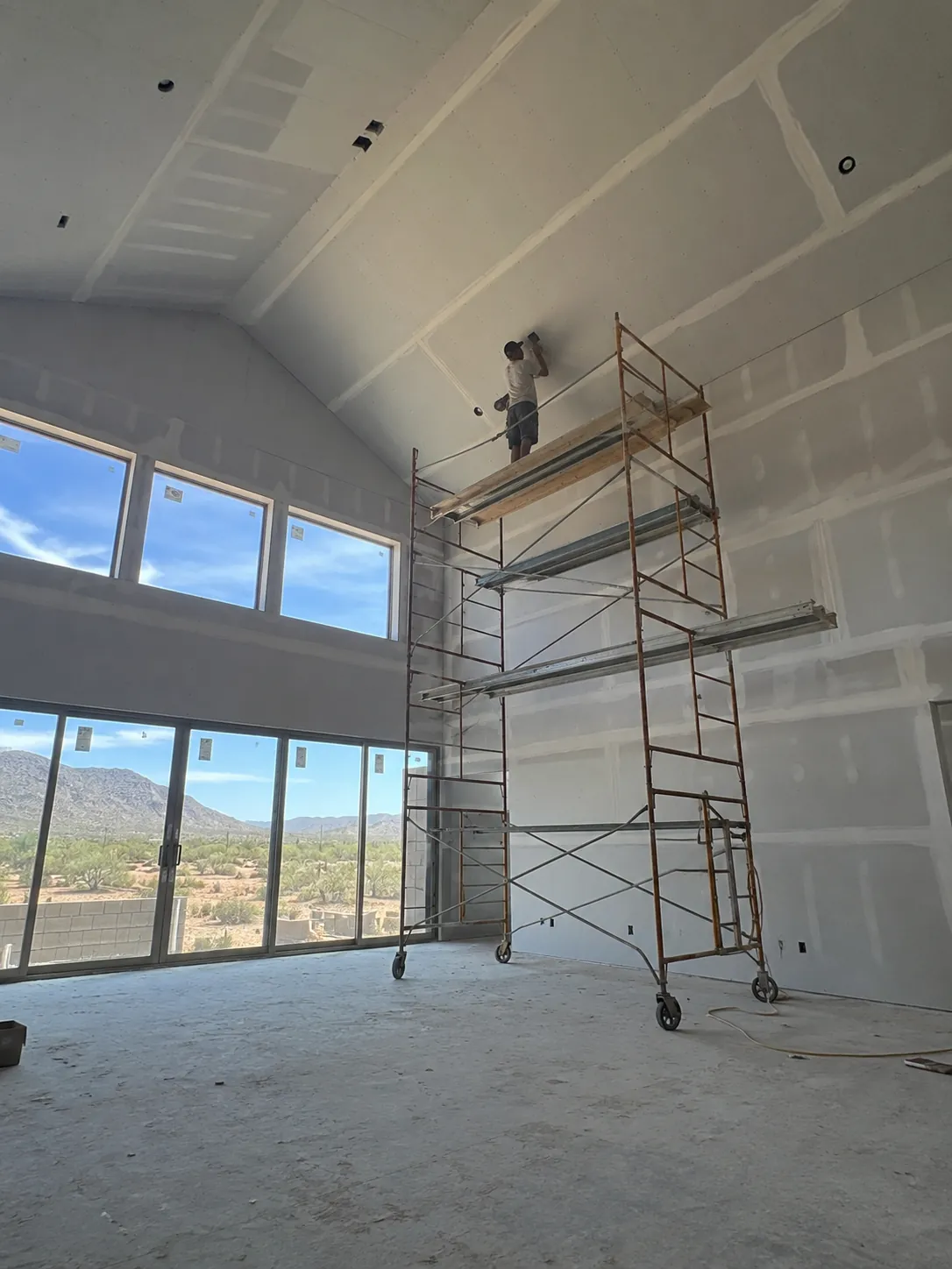 Drywall installation on a tall vaulted great-room ceiling in a new build